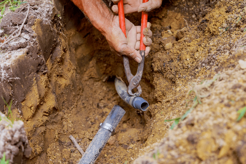 Worker installing sprinkler system pipes in residential yard during setup