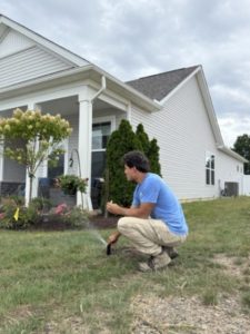 Technician performing irrigation system inspections before winter by checking a residential sprinkler head.