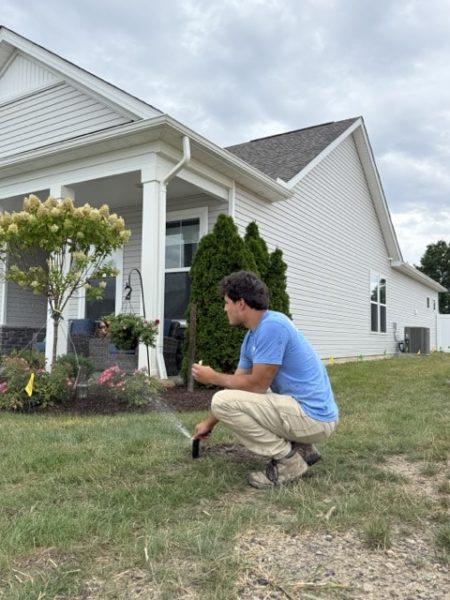 Technician performing irrigation system inspections before winter by checking a residential sprinkler head.